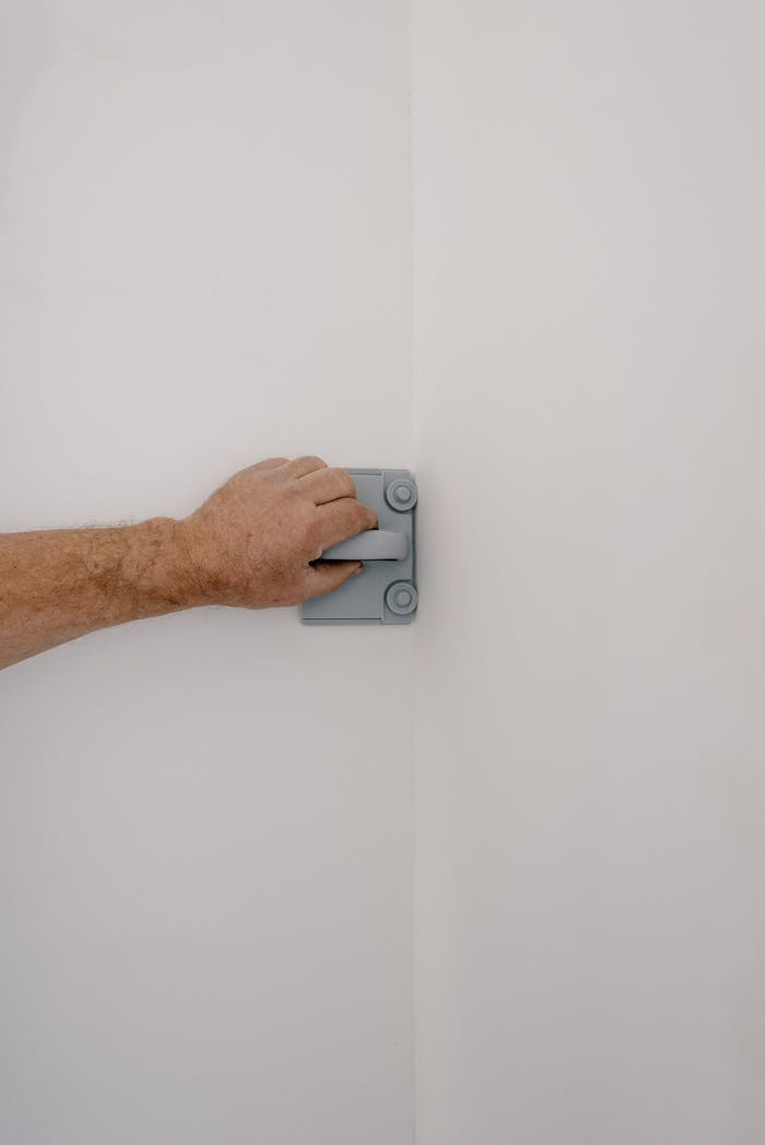 A close-up of a hand using a sanding tool on a wall during a home renovation.